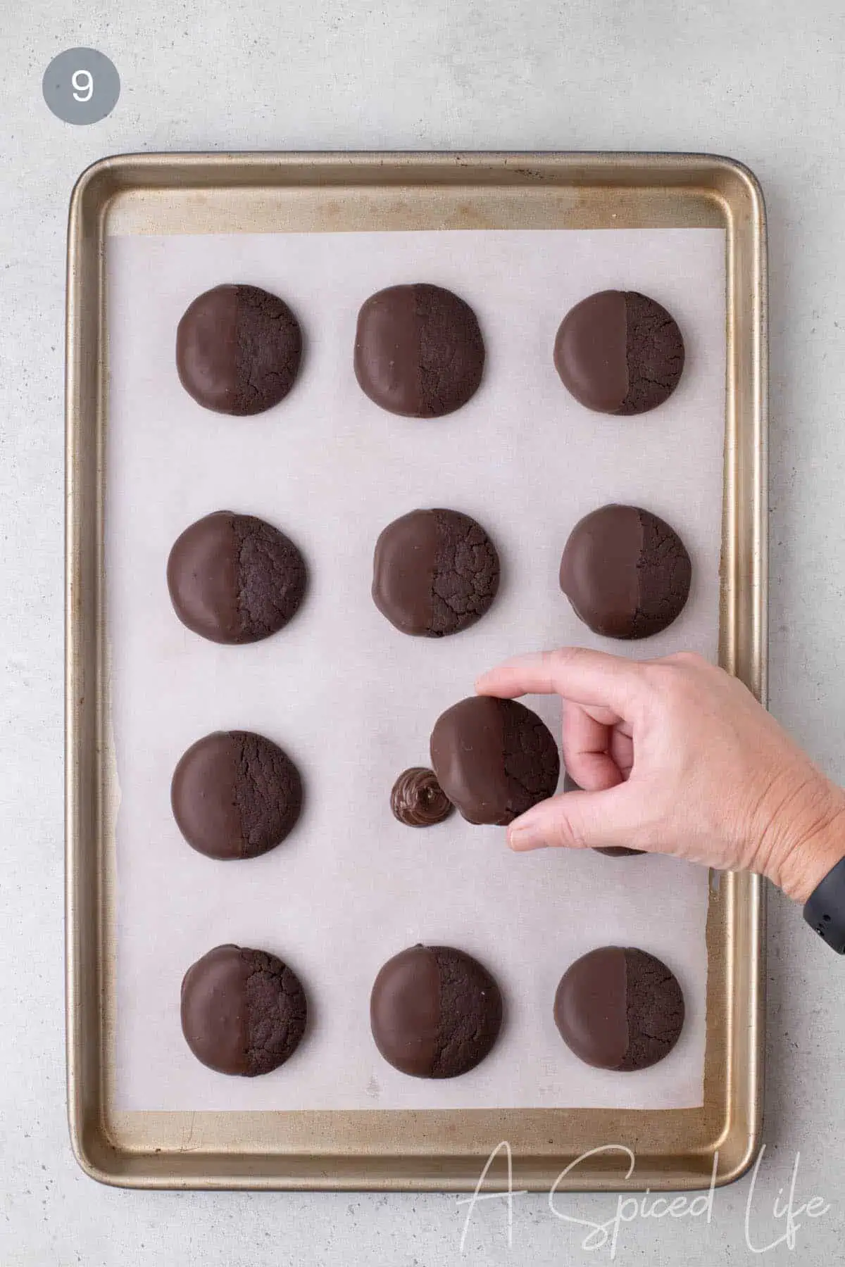 Hand placing a half-dipped chocolate cookie onto a small mound of melted chocolate on parchment.