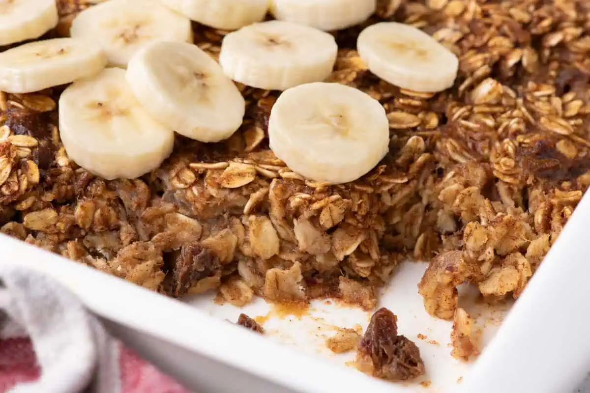 Close-up of partially served banana baked oatmeal, showing individual rolled oats and date pieces beneath banana slices.