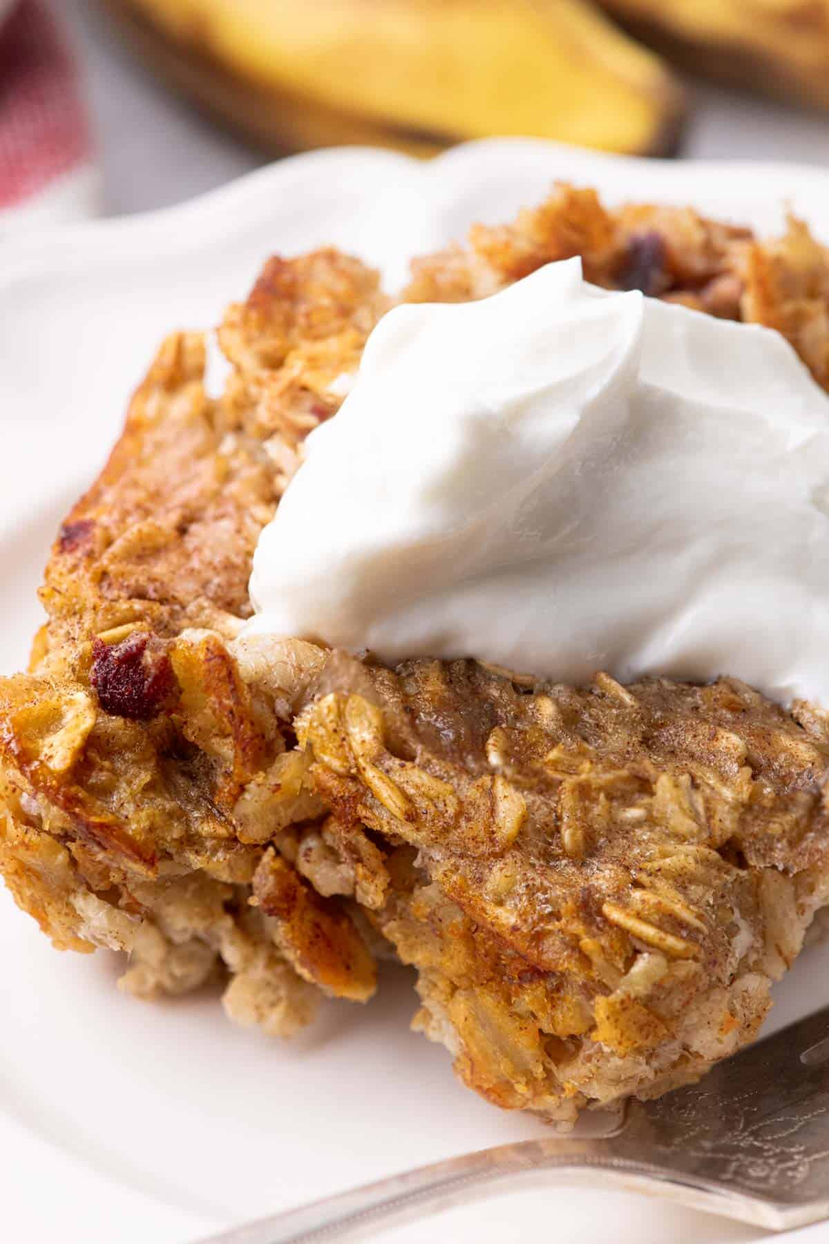 A serving of banana-and-date baked oatmeal, topped with a dollop of Greek yogurt, on a white plate.