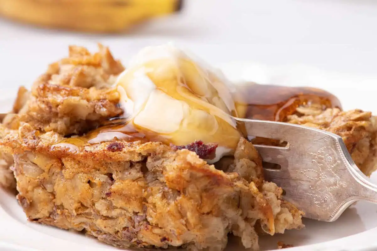 Close-up of banana bread oatmeal topped with Greek yogurt and maple syrup, with a fork breaking into the serving.