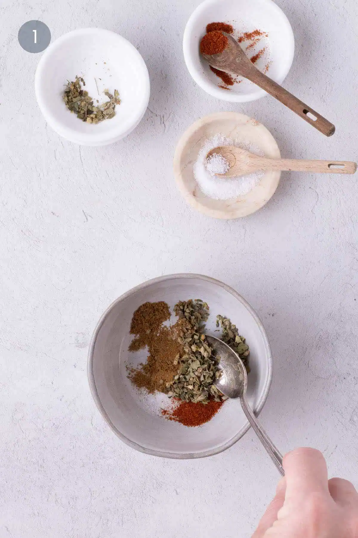 Mixing salt, cumin, oregano, and cayenne in a small bowl for chicken and vegetable sheet pan.