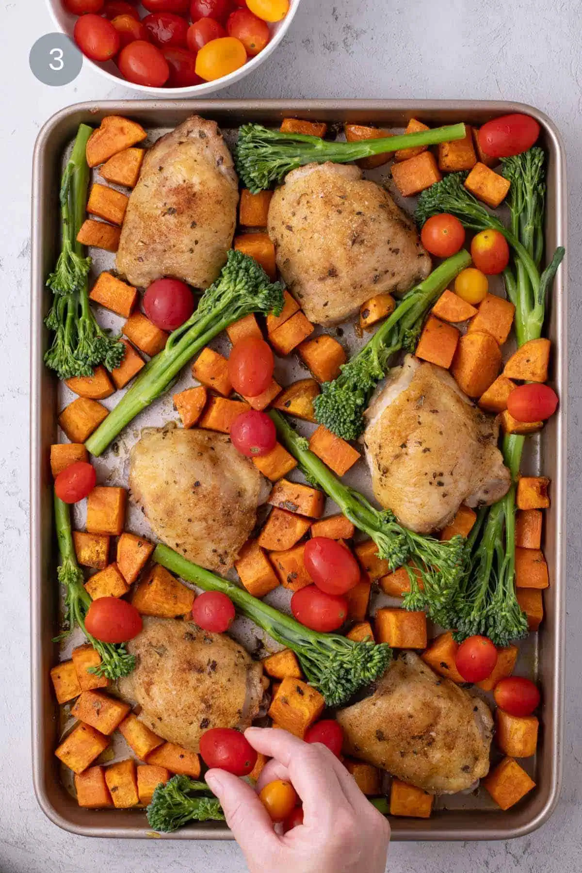 Partially roasted chicken thighs and sweet potatoes with broccolini and cherry tomatoes added to the sheet pan.