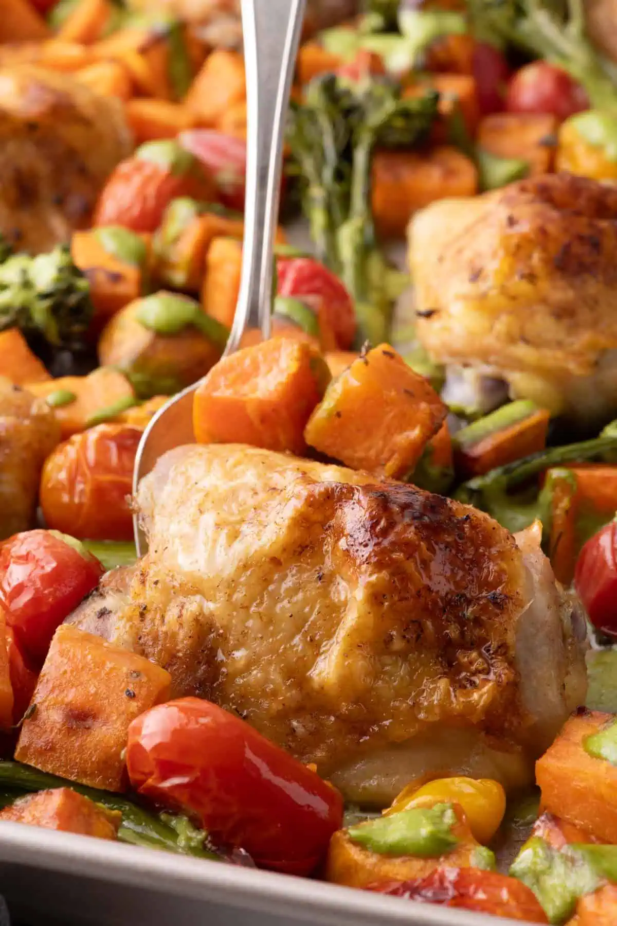 Close-up of crispy roasted chicken thigh with sweet potatoes, cherry tomatoes, broccolini, and cilantro cashew pesto.