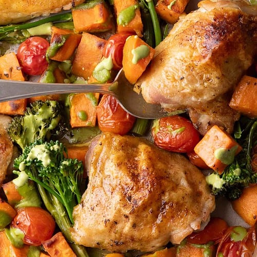 Crispy chicken thighs with roasted sweet potatoes, broccolini, and cherry tomatoes drizzled with cilantro cashew pesto on a sheet pan