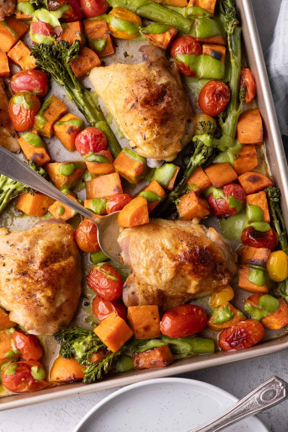 Chicken and vegetable sheet pan with crispy chicken thighs, sweet potatoes, broccolini, tomatoes, and cilantro cashew pesto.