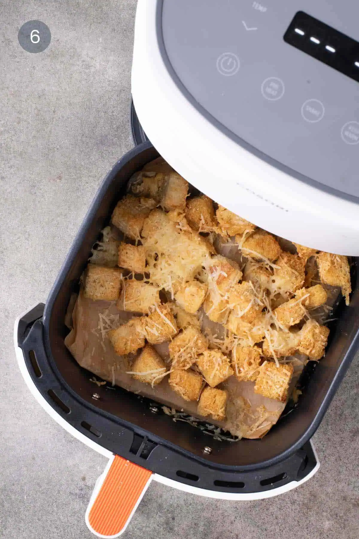 Golden bread cubes with melted cheese and browned cheese edges in a parchment-lined air-fryer basket.