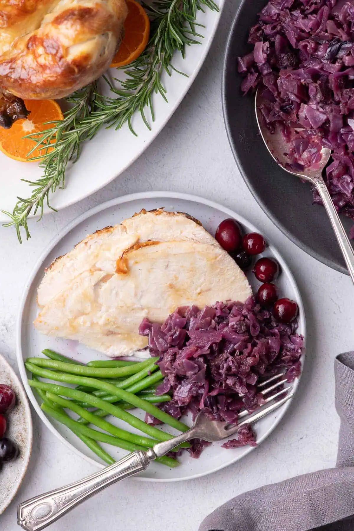 German braised red cabbage served with sliced turkey breast, green beans, and cranberries on a white plate.