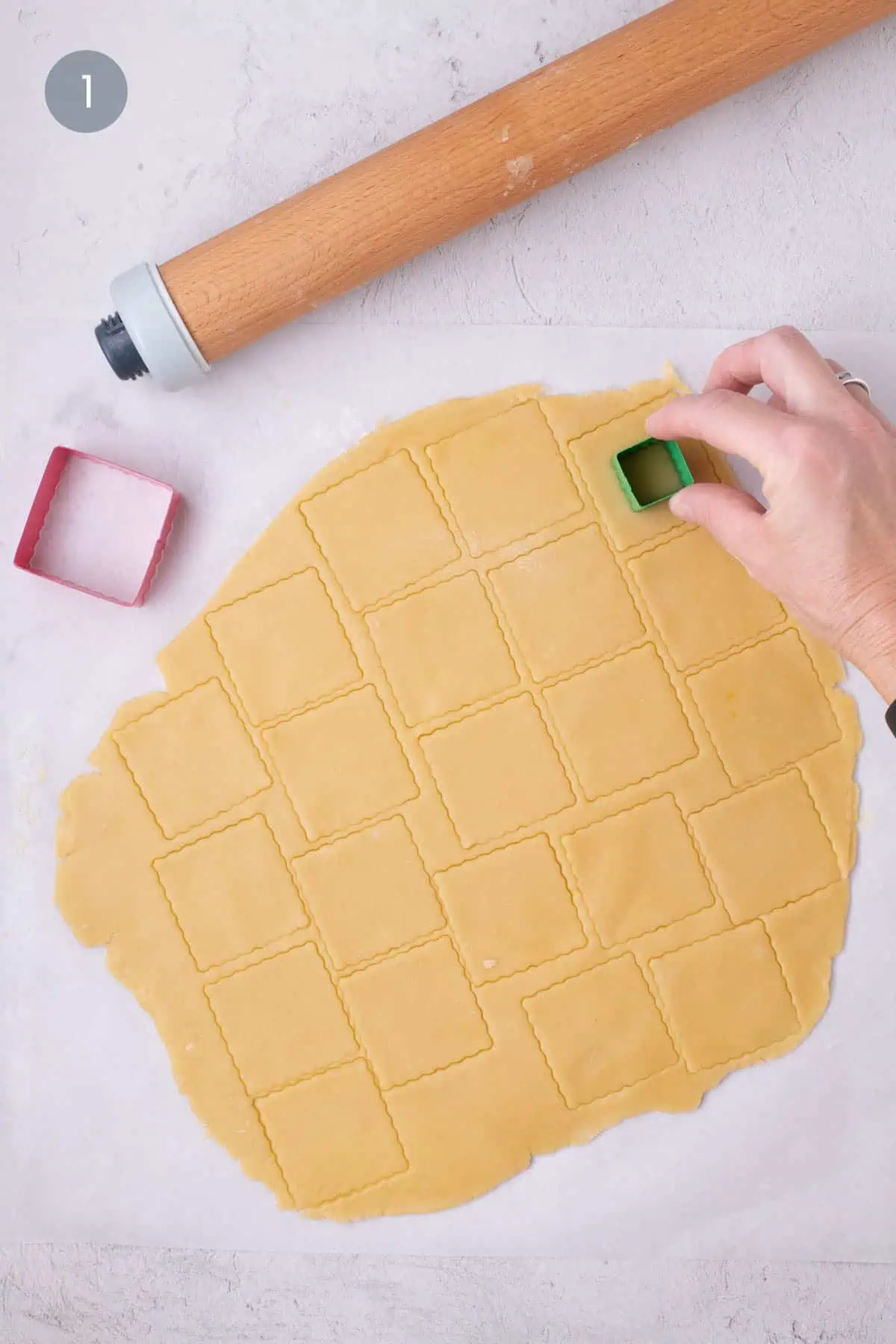 Hand cutting fluted square cookies from rolled dough on parchment paper.