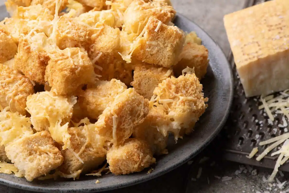 Close-up of golden sourdough croutons with melted cheese and crisp edges beside a Parmesan wedge.