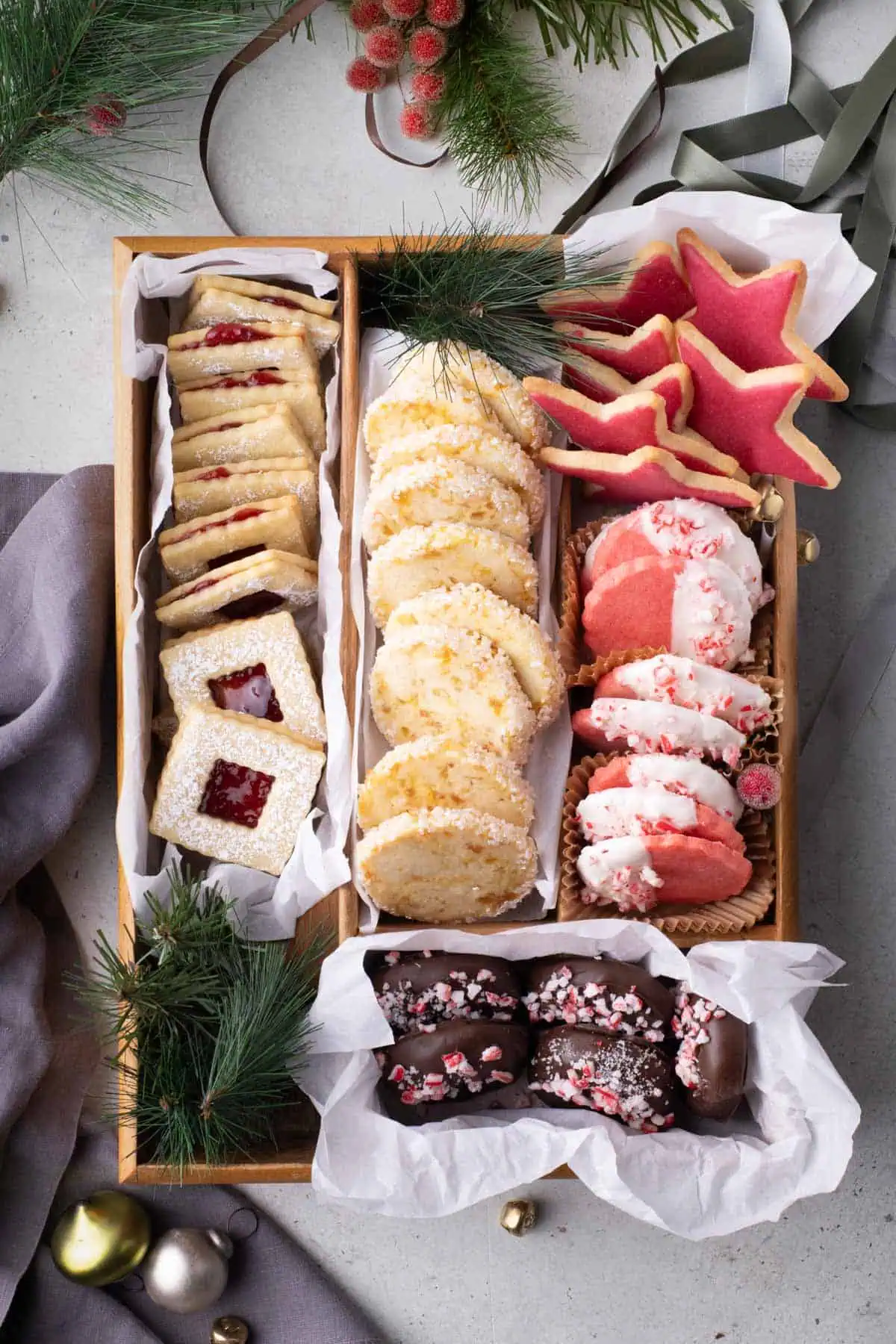 Finished Christmas cookie box with five varieties of homemade cookies arranged in a divided wooden tray with festive greenery