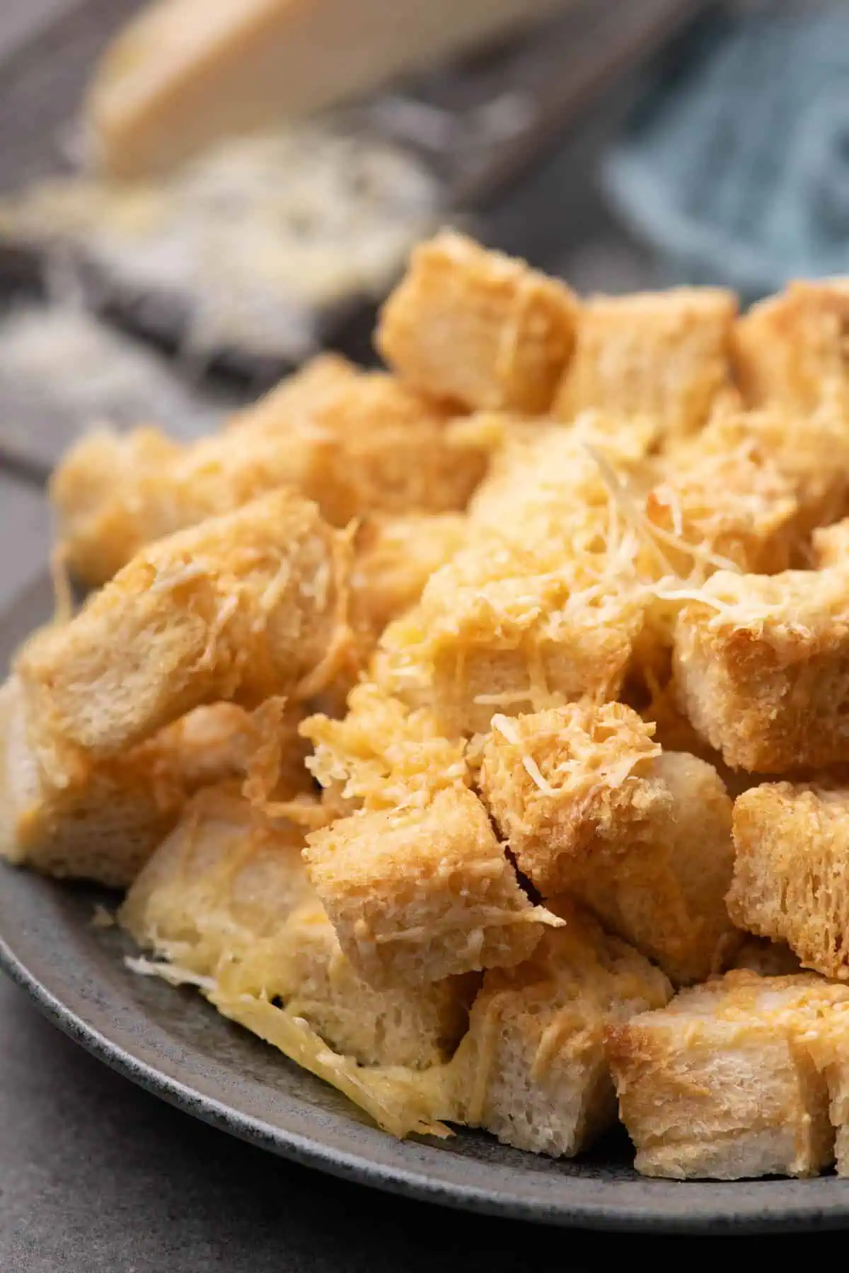Close-up of toasted bread cubes piled on a gray plate with golden cheese and lacy melted edges.