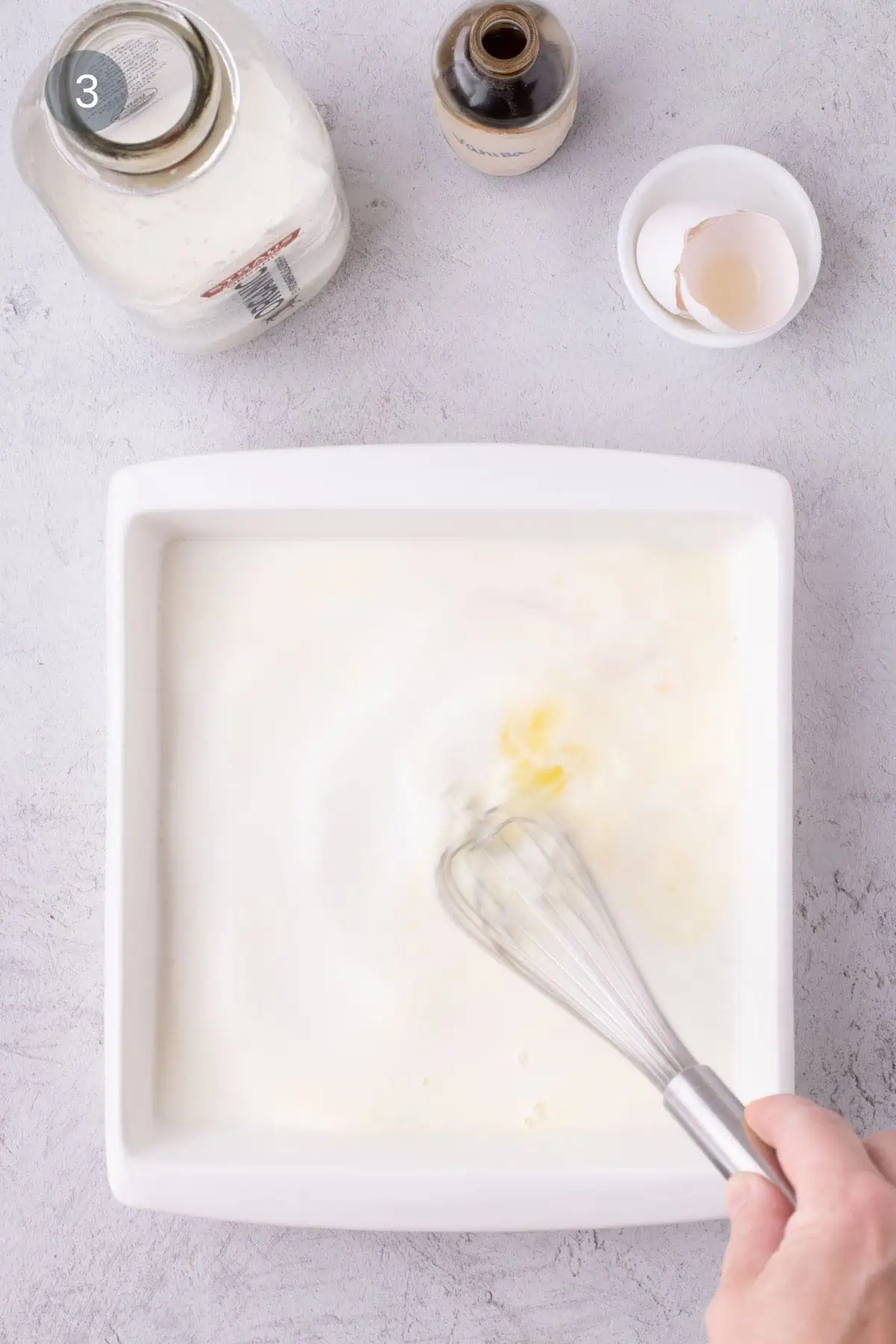 Milk, egg, and vanilla being whisked together in a white square baking dish.